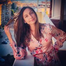 Yüksekçe bir balkonda, sağ dirseğiyle pervaza yaslanmış ve eliyle fönlü saçlarını tutmuş, çok hafif tebessüm ediyor, sol eli belinde, yavruağzı üzerine çiçekli bluzu var.